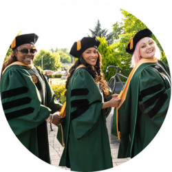 Three student are wearing graduation regalia. They smile toward the camera.